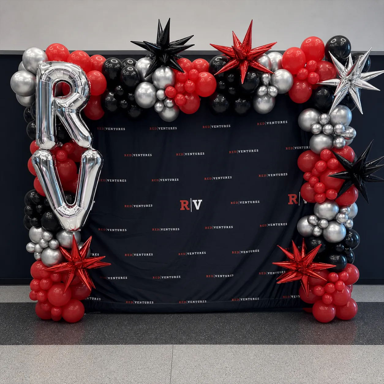Red, black, and silver balloon arch framing an event backdrop